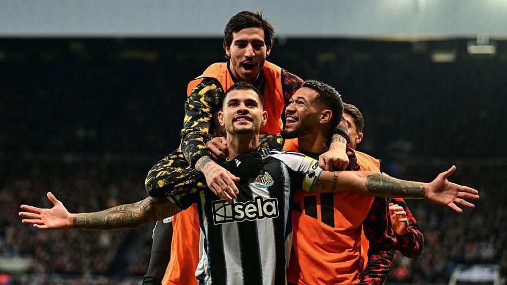 Bruno Guimaraes stands with his arms out celebrating, with Sandro Tonali and Joelinton with him