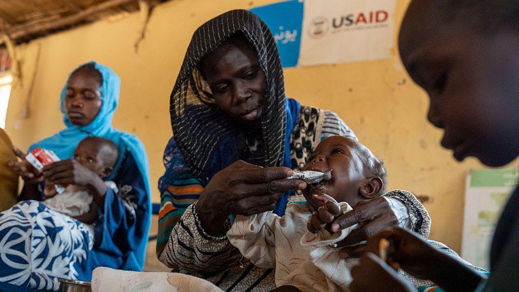 Woman feeds baby with USAID sign in background
