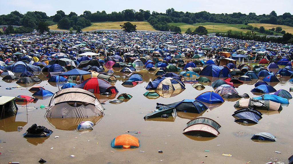 Hundreds of tents on a campsite that has been submerged in water, The water is brown with mud and there is litter floating in the water.