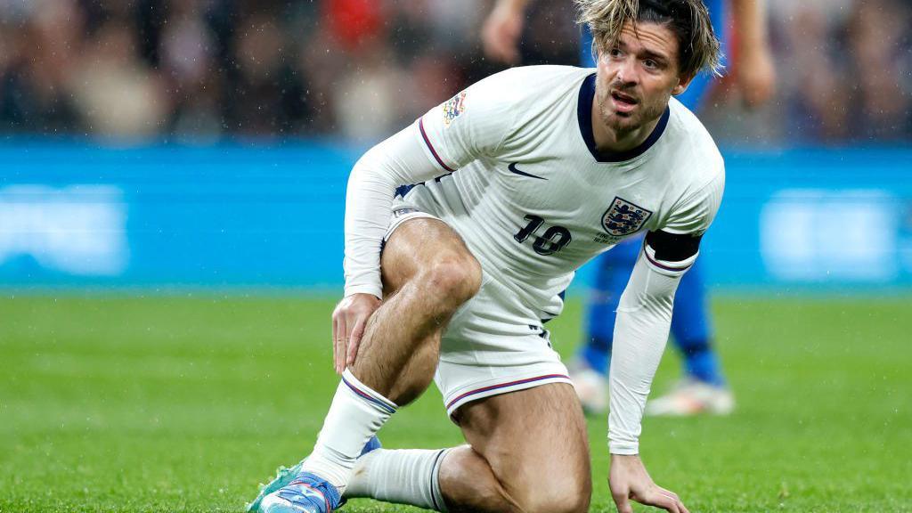 Jack Grealish holds his leg while kneeling on the floor after receiving a kick