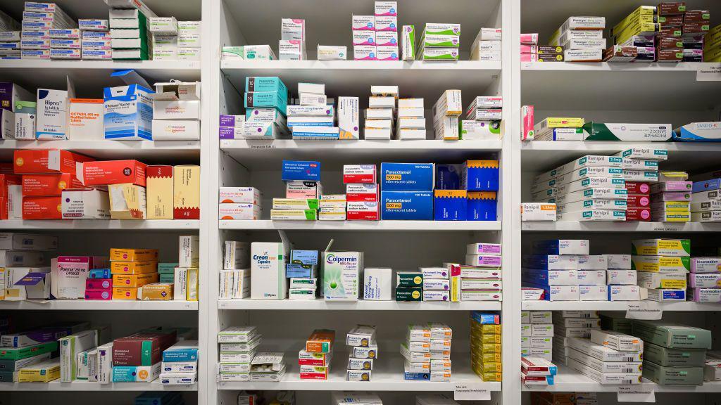 A set of shelves in a pharmacy, with different medications stacked and organised by type.
