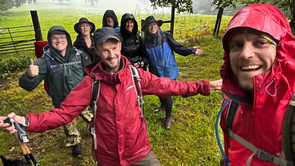 Jamie Rudd surrounded by six people all in wet-weather gear in a field and putting their thumbs up