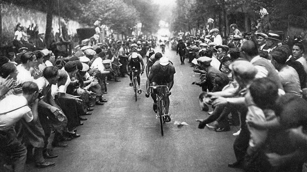 Black and white photo of Tour de France cyclists and cheering crowd.