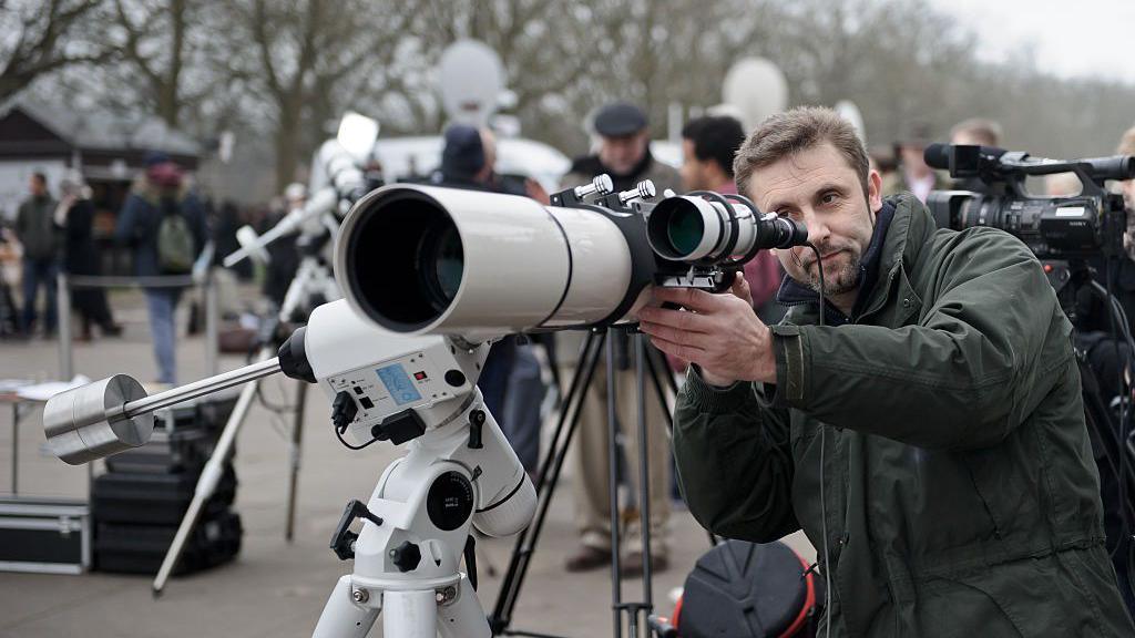 Man looks through a telescope during a public solar eclipse viewing event in London.