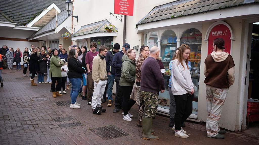 Trigolion yn ciwio y tu allan i Siop 'Paws Pet' er mwyn casglu a gwarchod pysgod, ar ol apel ar gyfryngau cymdeithasol yn gofyn i achub y pysgod cyn i'r trydan gael ei ddiffodd.