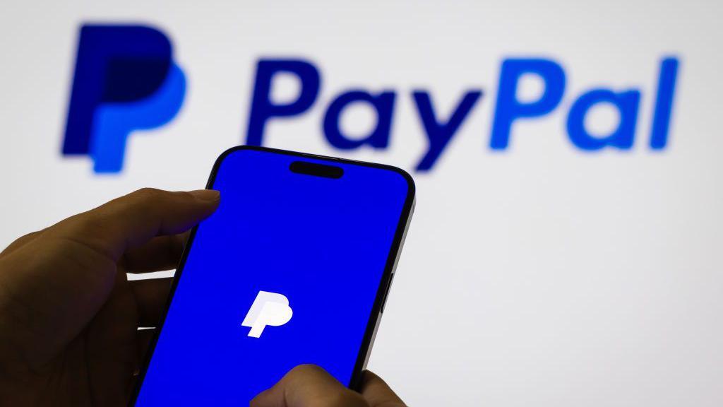 PayPal's logo displayed on a smartphone, with a larger logo shown on a white background behind it.