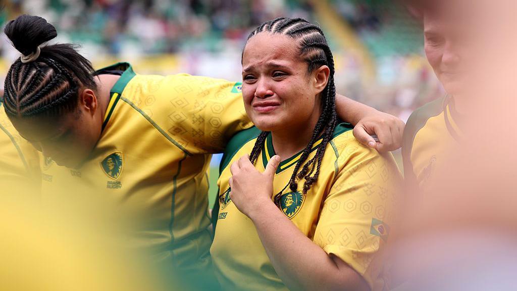 A Brazilian rugby player in a yellow shirt. She is emotional and close to tears.