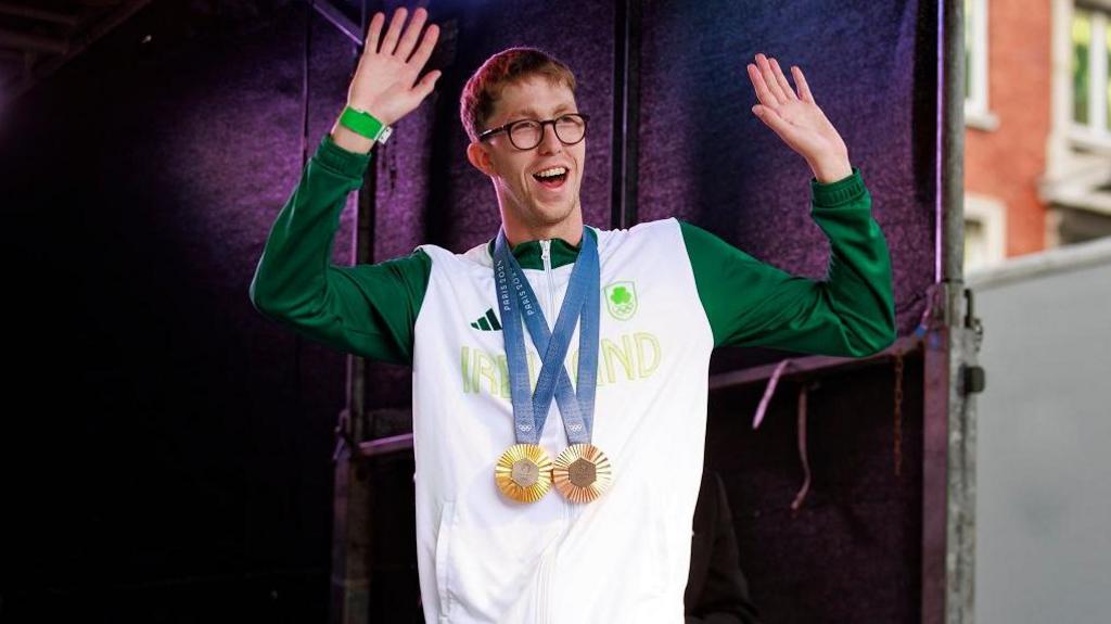 Daniel Wiffen on stage with his gold and bronze medals around his neck 