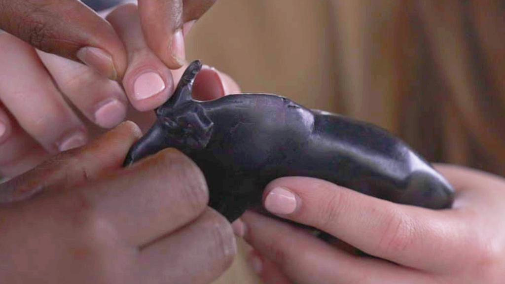 William guides Lucy's fingers over a wooden model of a wildebeest