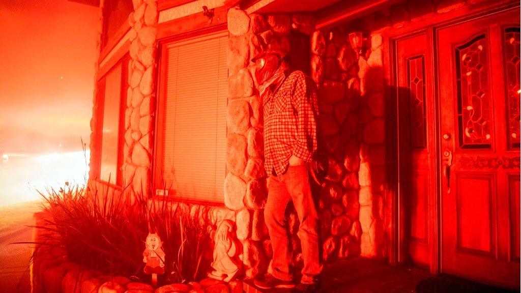 A man watches his neighbours's home burn from his front porch during the Hillside fire