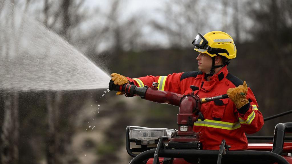 A Surrey firefighter in red and yellow firefighting kit manning a water hose