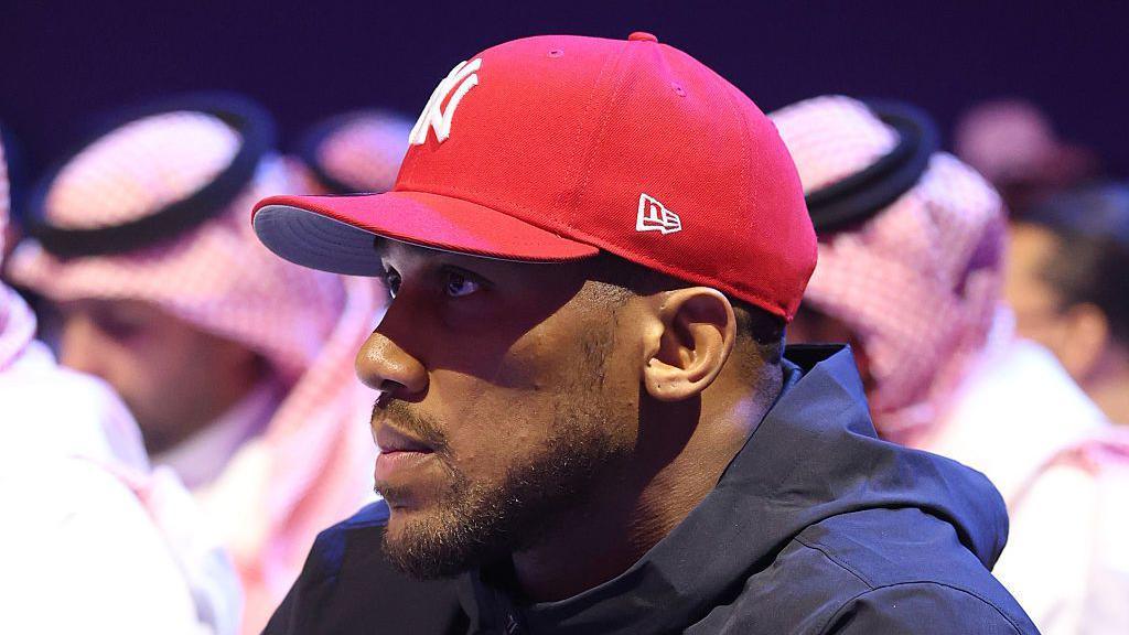 Anthony Joshua looks on at ringside in a red cap