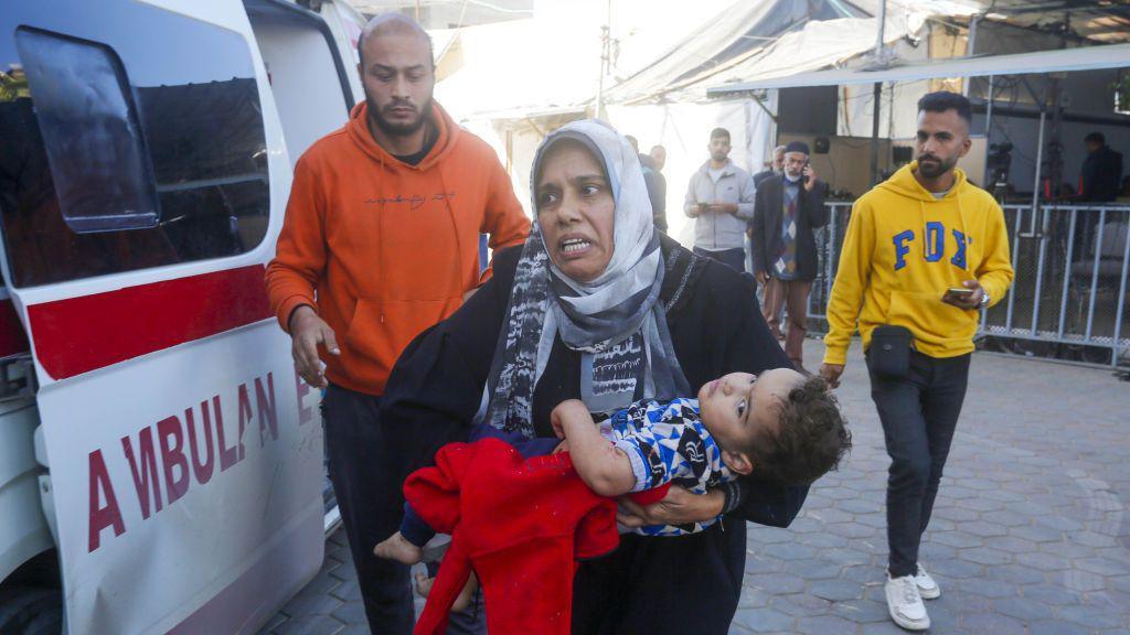 A Palestinian woman carries an injured child into Al-Aqsa Martyrs Hospital following an Israeli air strike in Nuseirat refugee camp, in central Gaza (4 December 2024)