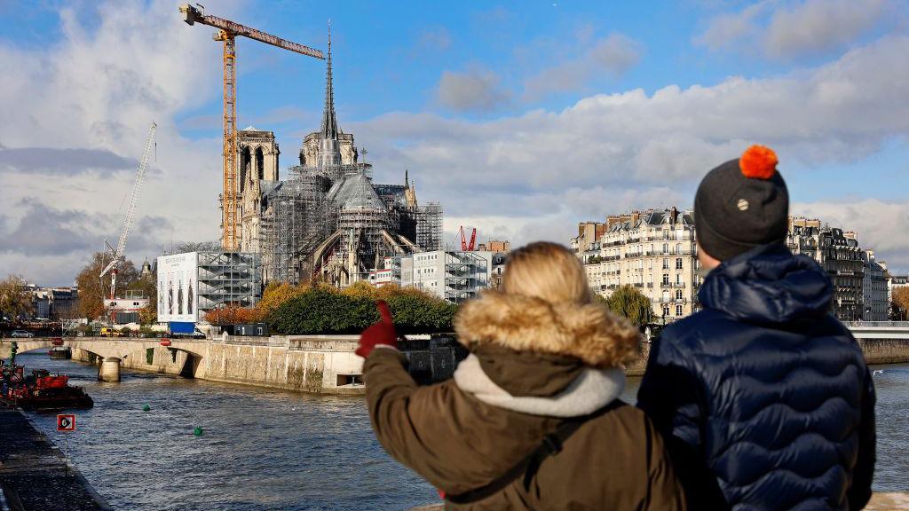 People look at Notre Dame under scaffolding