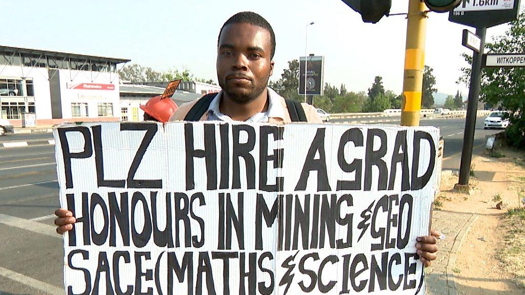 Jobless graduate Brian Radzuma holds a sign