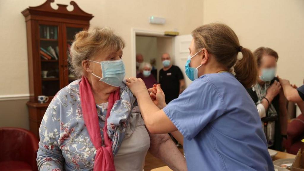 An elderly woman receives a vaccine by a nurse in a nursing home