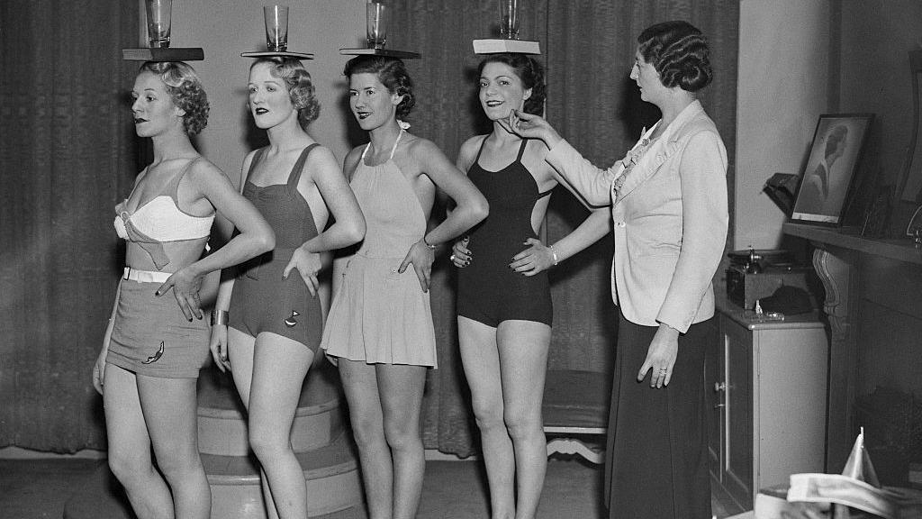 Sylvia Lucie Golledge (right) instructs pupils in the art of correct posture by balancing a glass and book on their heads at her modelling agency and finishing school in Old Cavendish Street, London, 25th November 1936. 