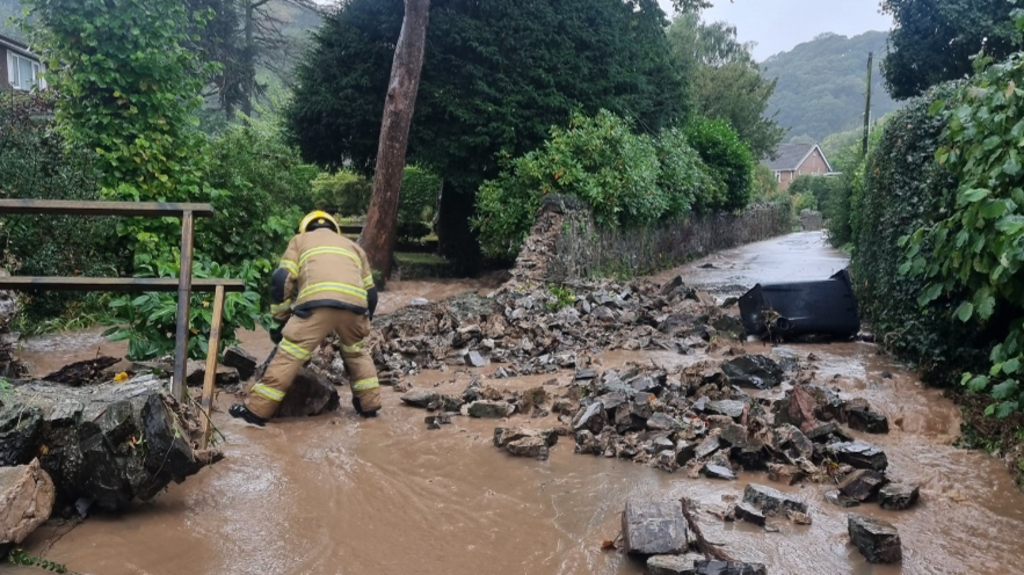 A firefighter next to a broken wall with flood water down it