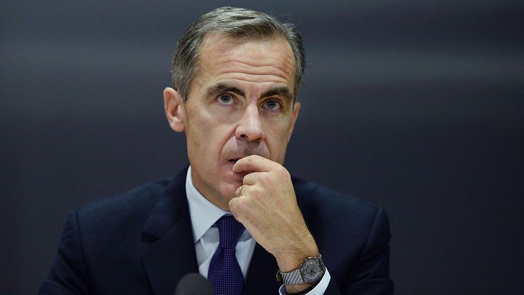 Mark Carney, in a dark blue suit and tie and light shirt, listens during the Bank of England's Financial Stability Report press conference at the Bank of England