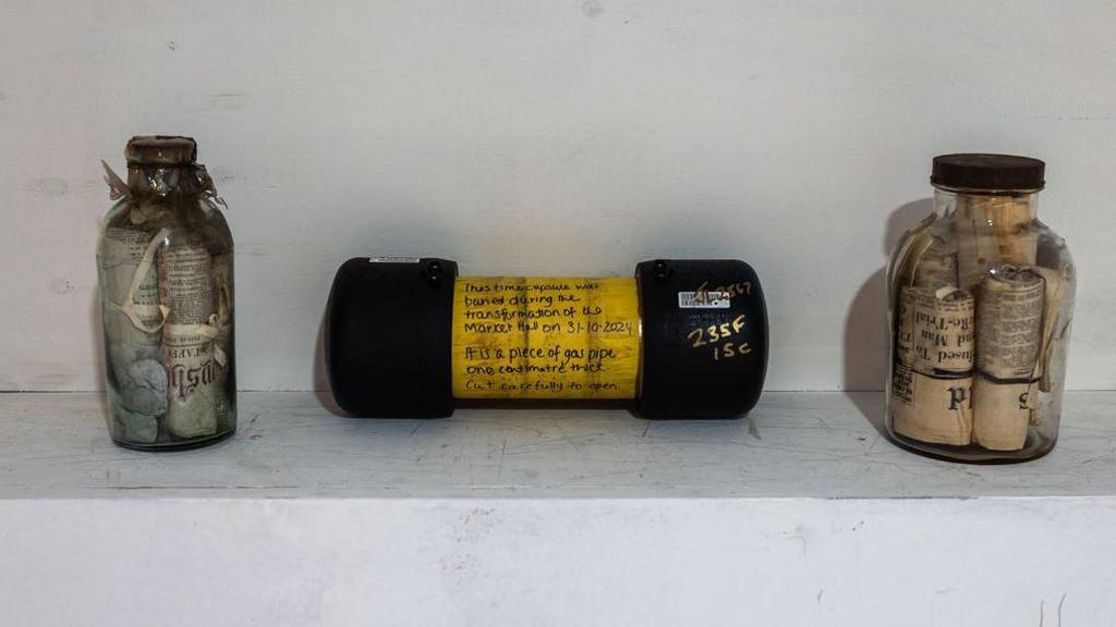 Two time capsules in glass bottles, dating from 1864 and 1938, next to a yellow time capsule from 2024