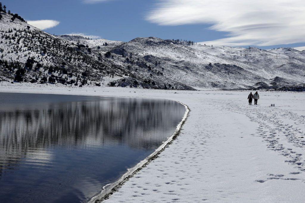 People take a stroll in the snow by Lake Sidi Ali. All of the landscape is covered in snow.