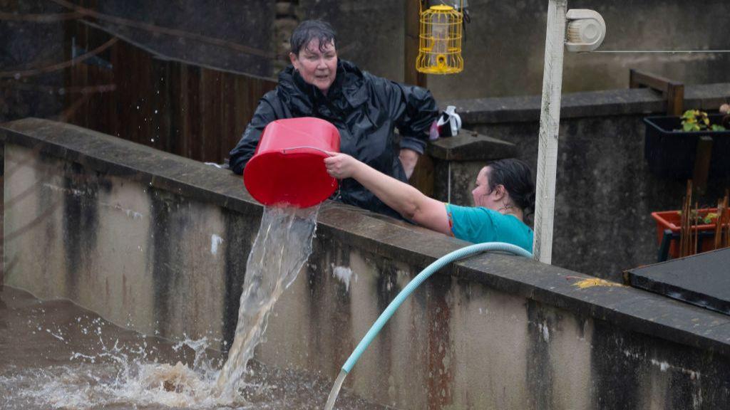 People bail water out of the front garden of properties using buckets