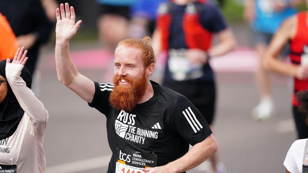 A ginger man running, wearing a black top. 