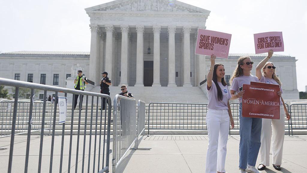 three women holding up signs that say "girls' sports for girls only" in front of Supreme Court building