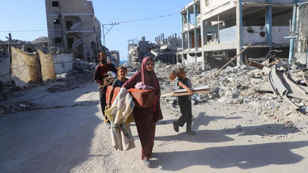 Displaced Palestinian woman Amal Alyan and her family walk past the rubble of their destroyed home, amid a ceasefire between Israel and Hamas