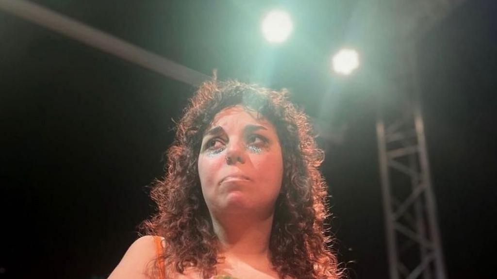 A girl with black curly hairs looks sad under stage lights