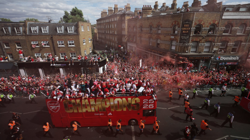 General view as Arsenal players and fans celebrate during the victory parade. Red bus with Arsenal FC players in the foreground surrounded by escorts, fans in the foreground in Arsenal shirts and flare smoke clouding parts of them