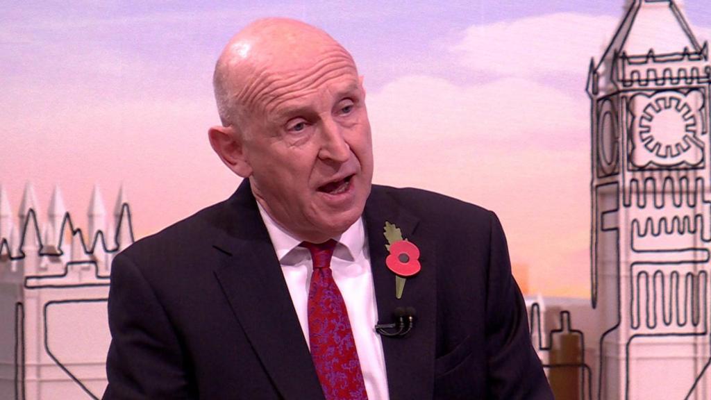 John Healey mid-speech in dark suit with poppy pin on his left lapel