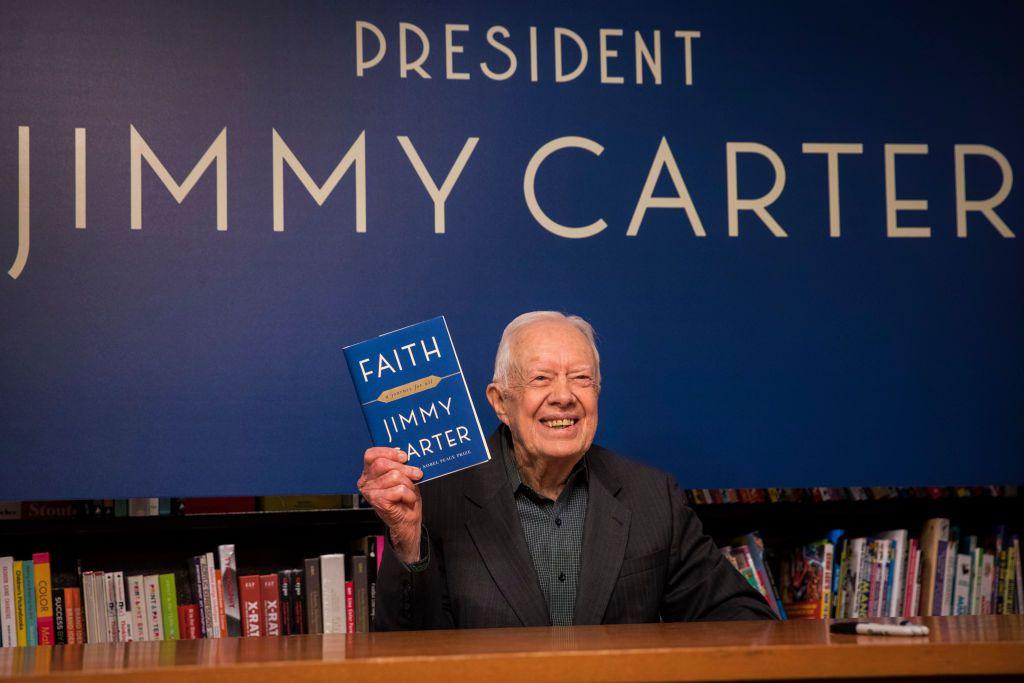 Carter holds up a copy of his book Faith: A Journey For All at a book signing event in New York in 2018