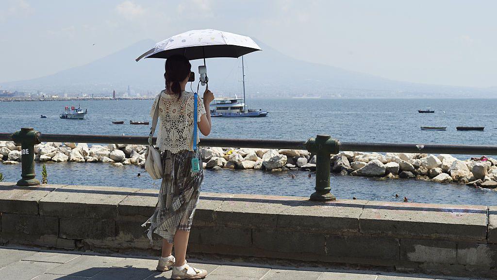 A woman uses an umbrella to shield herself from the sun during the African heatwave in Naples on August 4, 2026.