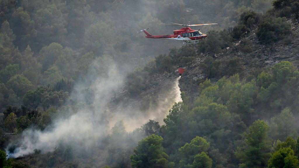 A firefighting helicopter dumps water over a wildfire near Betxi, 60 kilometres north of Valencia