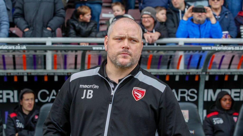 Morecambe manager Jim Bentley stands on the touchline while watching a game.