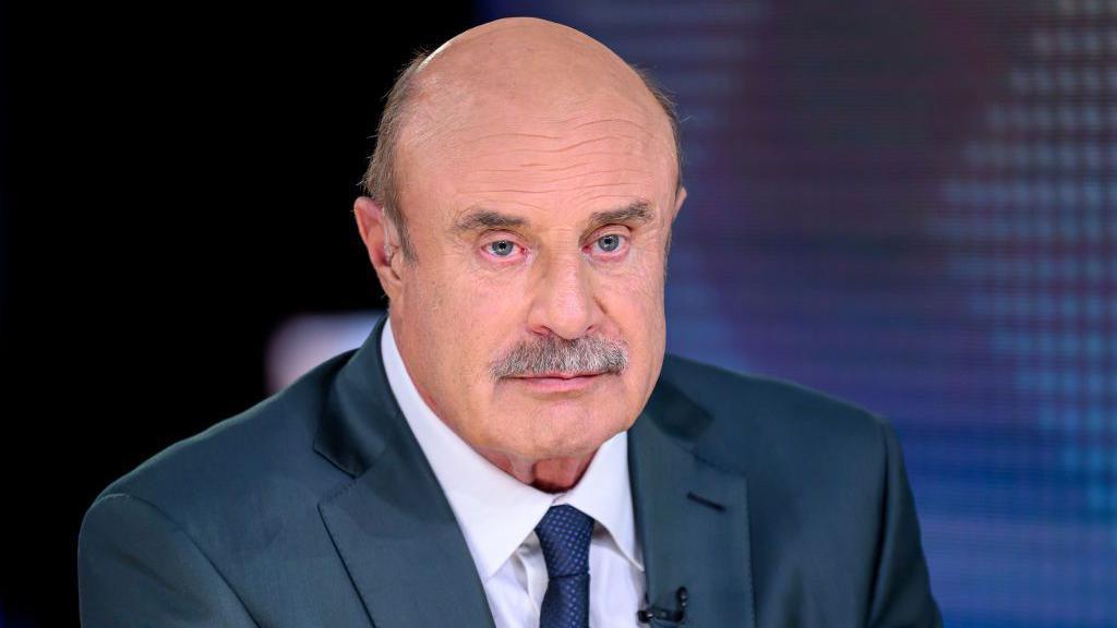A stock image of Dr Phil, who is wearing a navy suit and tie with a white shirt.