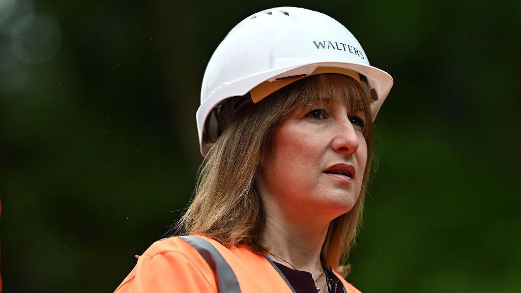 Llun o Rachel Reeves mewn siaced llachar a chap caled.