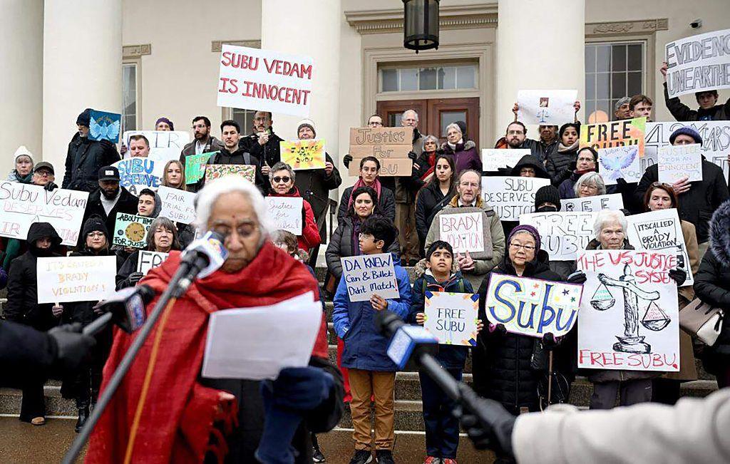 Saraswathi Vedam speaks at microphone outside courthouse as protestors gather with signs that read "Free Subu"