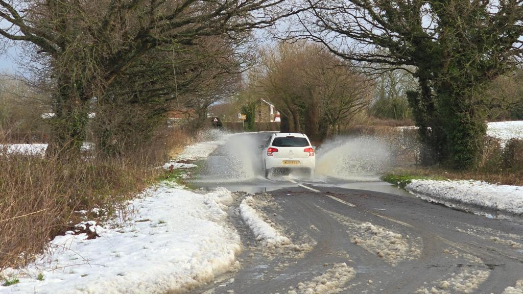 A car drives through a puddle on a snowy road