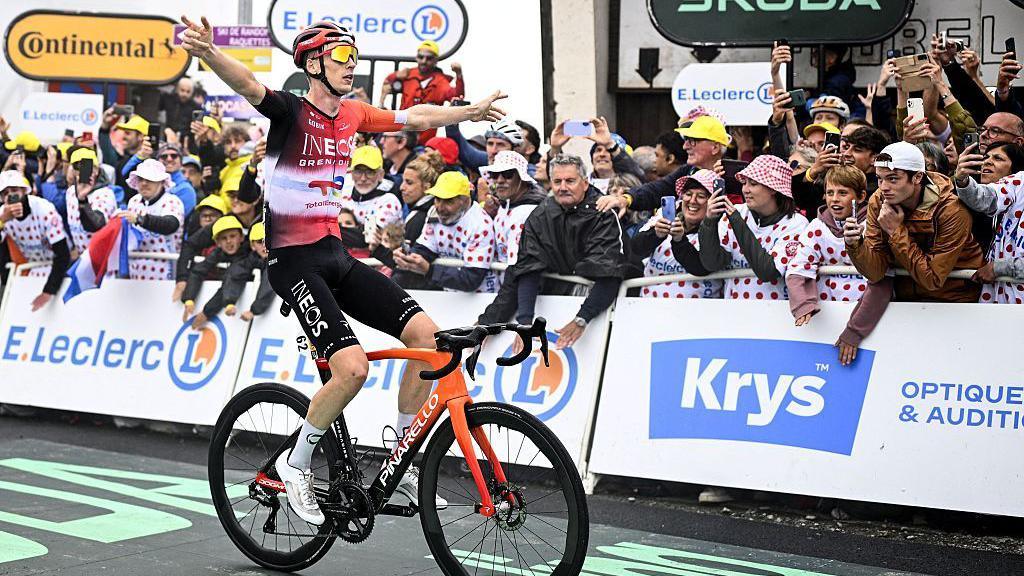 Thymen Arensman celebrates with his arms outstretched as he crosses the line at the end of stage 14