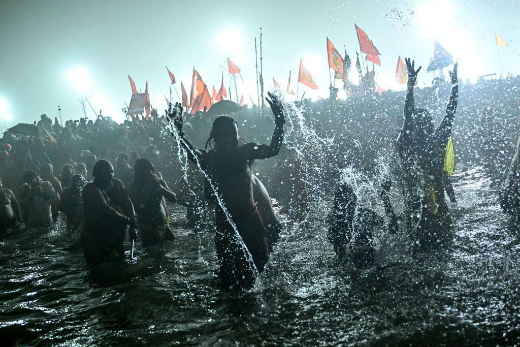 People take part in a mass bathing ritual in a river with flags waving in the background