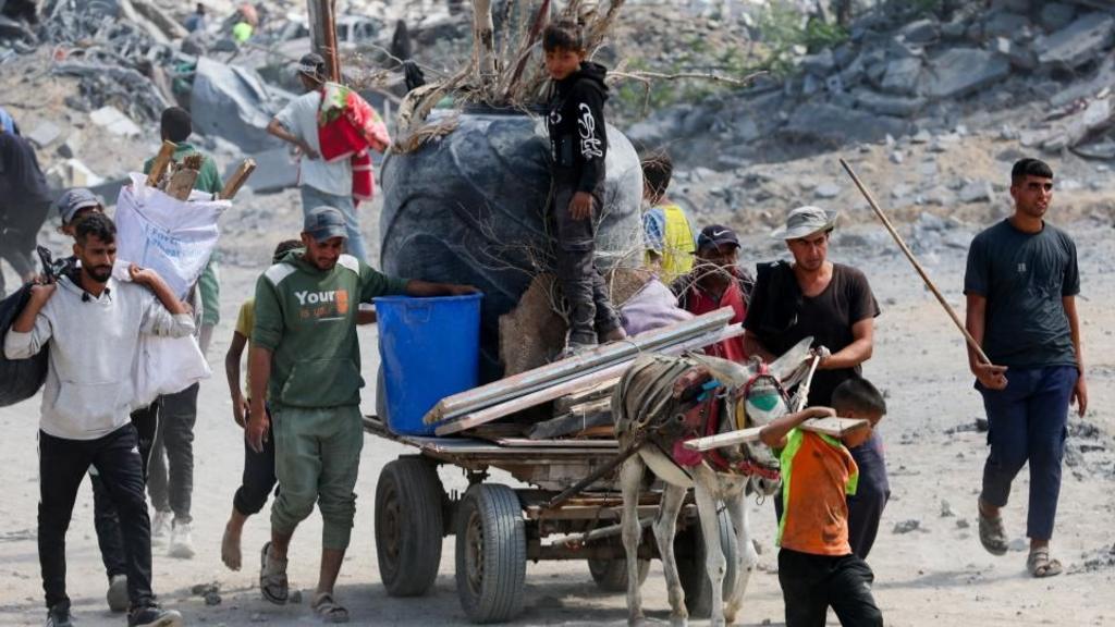 Palestinians pass by the rubble in Khan Younis, some carrying items on a donkey and cart