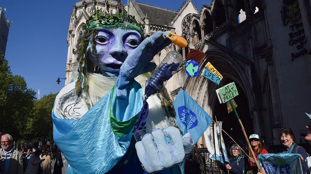 Llun o fodel a masg glas wedi'u dal yn yr awyr y tu allan i'r Uchel Lys yn Llundain
