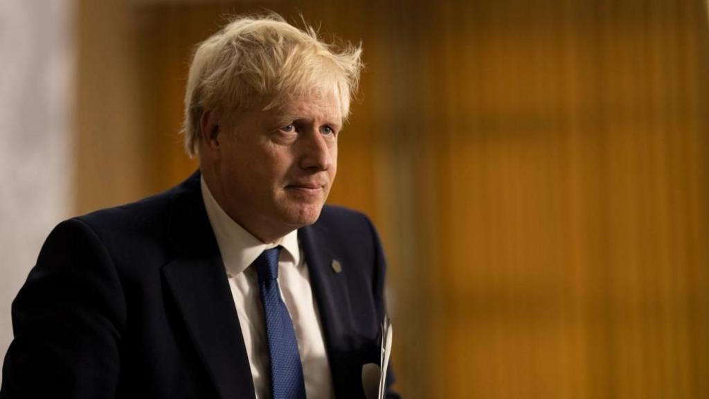 Former Prime Minister Boris Johnson is shown against a brown background carrying paperwork.