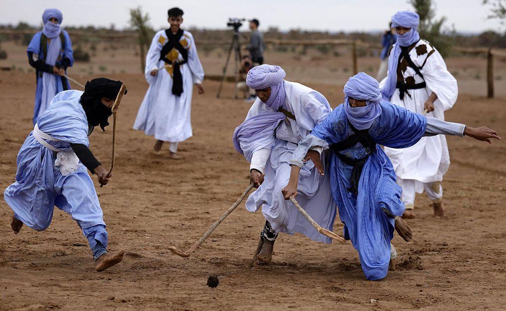 Men dressed in blue boubous and matching headwraps compete for the ball using wooden sticks.