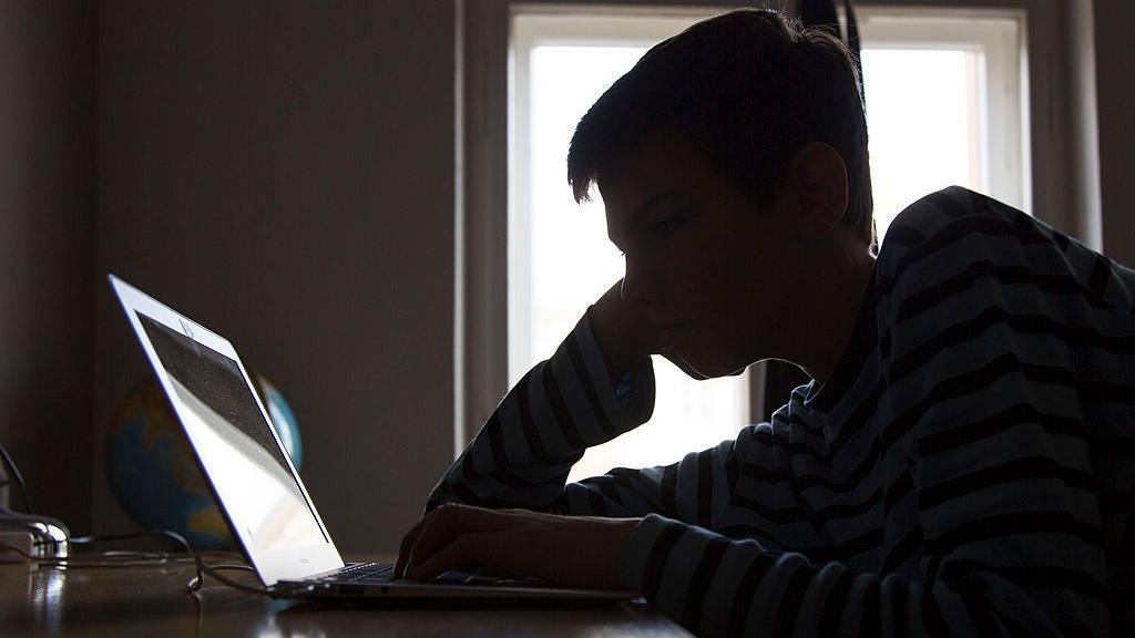 A silhouette of a boy reading the screen of a laptop