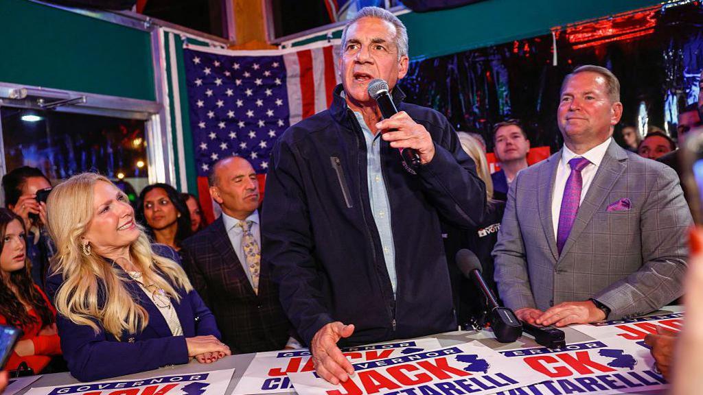 Republican gubernatorial candidate for New Jersey, Jack Ciattarelli, speaks during a campaign event while standing behind a table covered with campaign posters bearing his name.