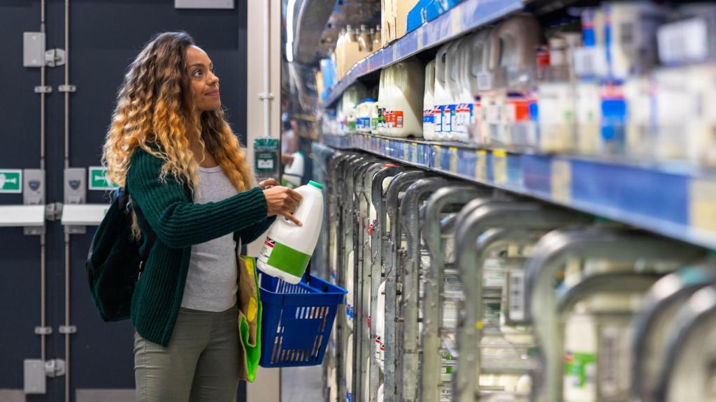 Mid-adult woman shopping on a budget. She is looking for low prices due to inflation, standing and holding a milk carton