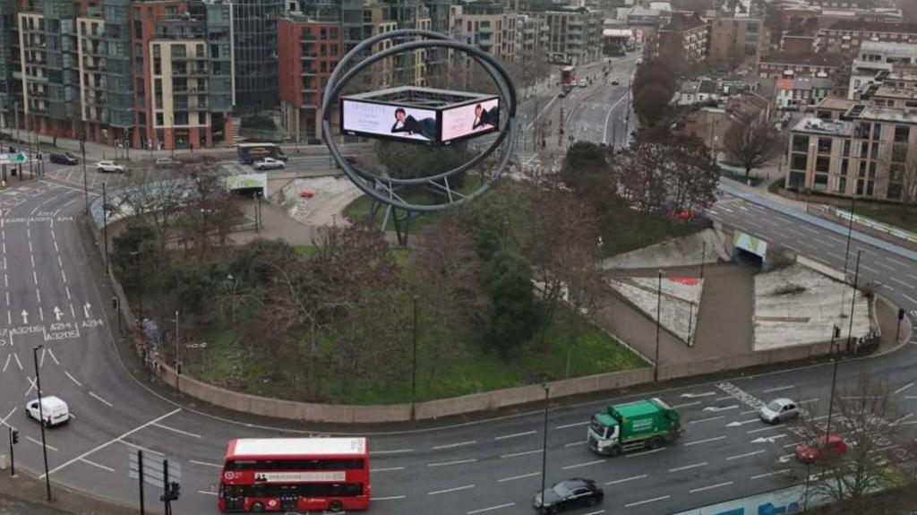 Current advertising structure shows screen in orb on roundabout with cars, bus and lorry